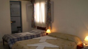Une chambre avec deux lits, une table de chevet avec une lampe, un miroir et une fenêtre avec des rideaux.
