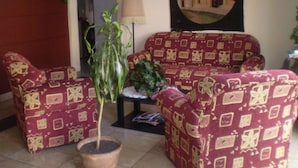 Un salon avec des meubles à motifs, une plante en pot, une lampe et une tapisserie murale.
