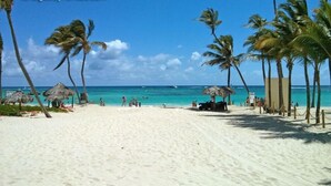A beach with white sand, palm trees, and a clear blue sea.