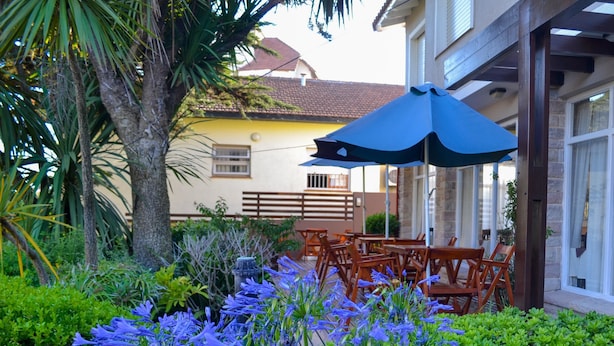 A garden with blue flowers and wooden chairs under a blue umbrella. - Hotel Rideamus (Villa Gesell)