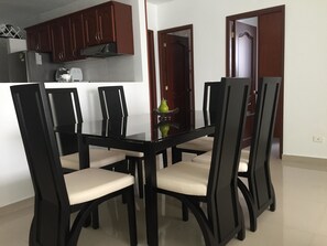 A dining area with a glass-top table and black chairs with beige cushions. - Edificio 7 Mares Apto 605 (Santa Marta)