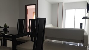 Moderni hotellihuone, jossa on ruokapöytä, tuoleja, sohva ja suuri ikkuna.