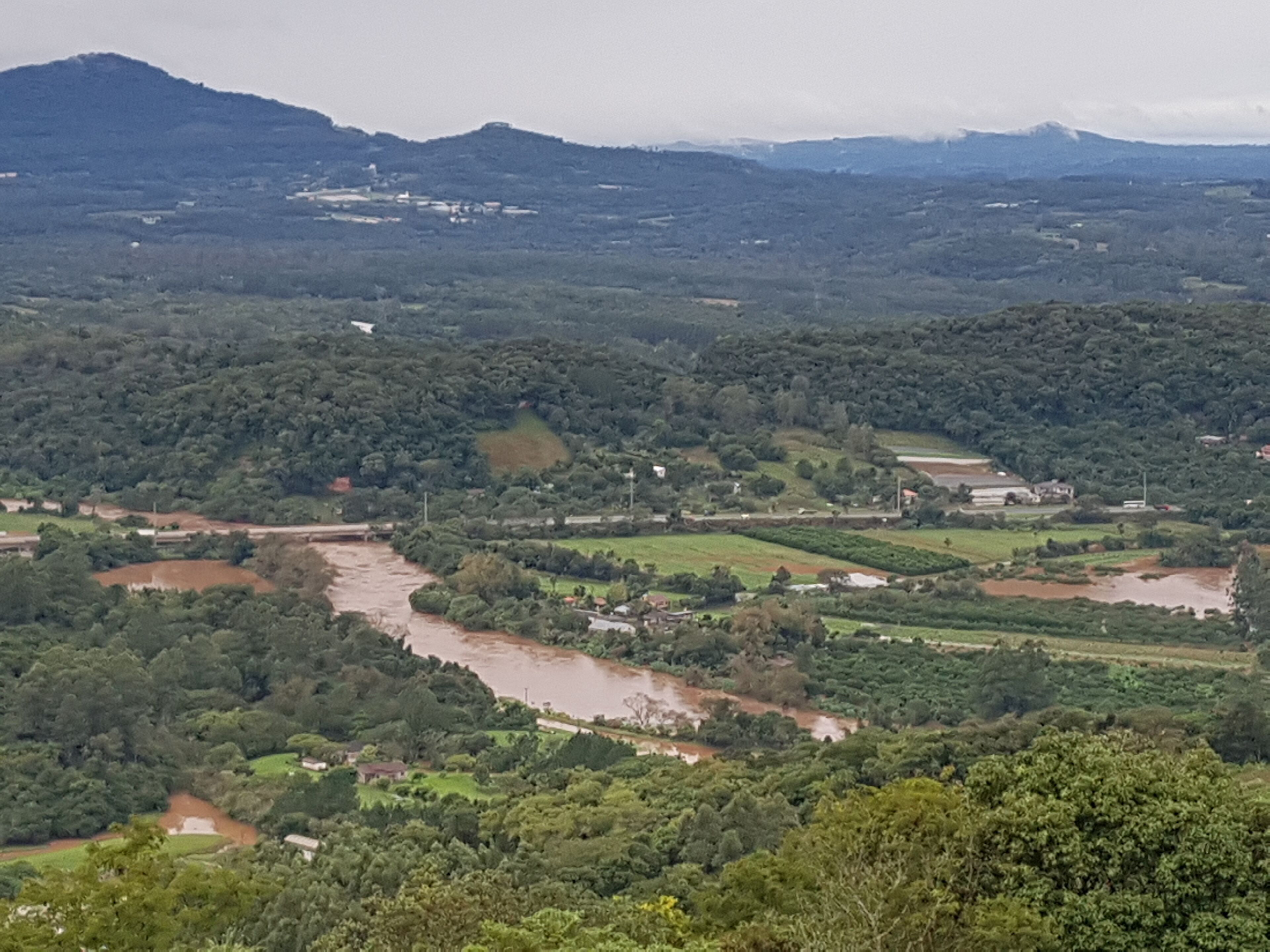 A river flowing through a valley with surrounding greenery and distant mountains.