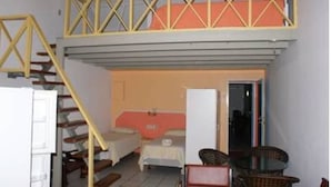 A room with a bed, a chair, and a table. There is a staircase with a railing leading to an upper level. - Green Hill Saliña Inn (Curaçao)