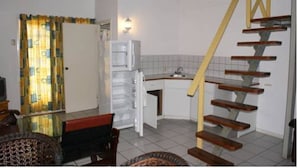 A kitchen with a white refrigerator, a wooden staircase, and a patterned curtain. - Green Hill Saliña Inn (Curaçao)