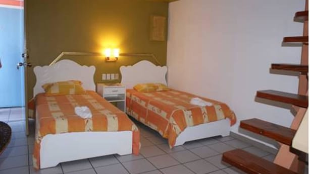 A room with two beds, a nightstand, a wall-mounted lamp, and a staircase. - Green Hill Saliña Inn (Curaçao)