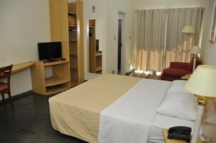 A hotel room with a bed, a desk with a TV, a chair, a wardrobe, and a red armchair.
