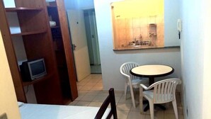 Um quarto pequeno com uma cama, uma televisão, uma mesa e cadeiras, e um espelho.