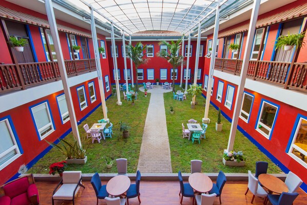 Un patio central con un sendero, rodeado de mesas y sillas, y balcones con plantas en macetas.