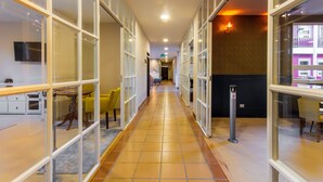 A corridor with glass partitions, a tiled floor, and a dining area with yellow chairs.