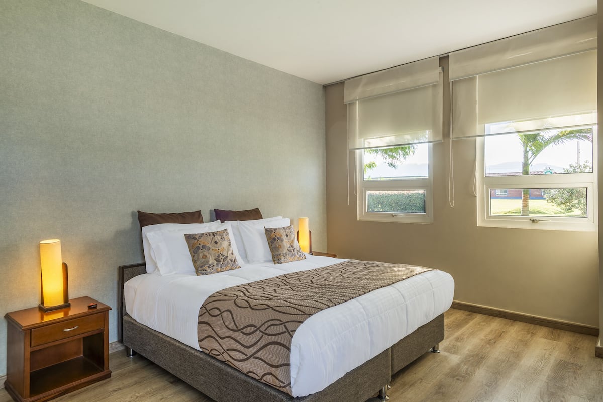 Un lit bien fait, recouvert d’une couvre-lit à motifs, avec deux lampes de chevet et une table de chevet dotée d’un tiroir.