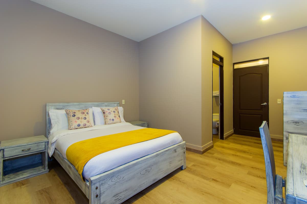 Une chambre à coucher avec un lit en bois, une table de chevet, une commode, un miroir et une porte.