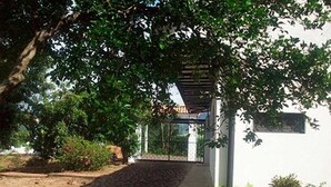Un chemin menant à un bâtiment doté d’une entrée couverte, entouré de verdure et bordé d’un mur blanc.