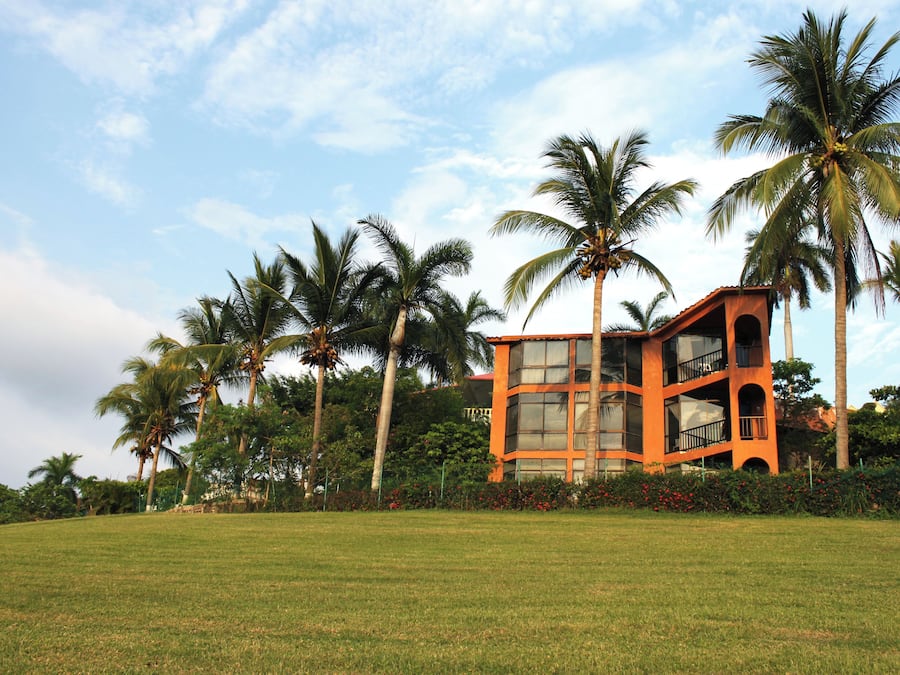 A modern building with large windows and a flat roof, surrounded by a well-maintained lawn and palm trees.