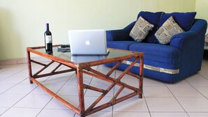 Ein Zimmer mit einem Holztischchen, einem Laptop, einer Weinflasche und einem blauen Sofa mit gemusterten Kissen.