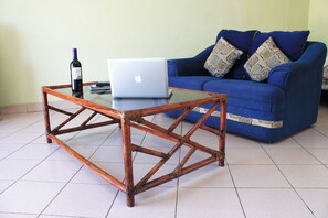 Um quarto com uma mesa de centro de vidro, um laptop e uma garrafa de vinho.