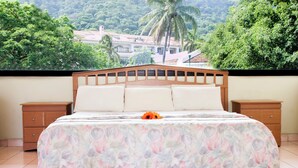 Ein Schlafzimmer mit einem Bett, zwei Nachttischen und Blick auf eine üppige grüne Landschaft.
