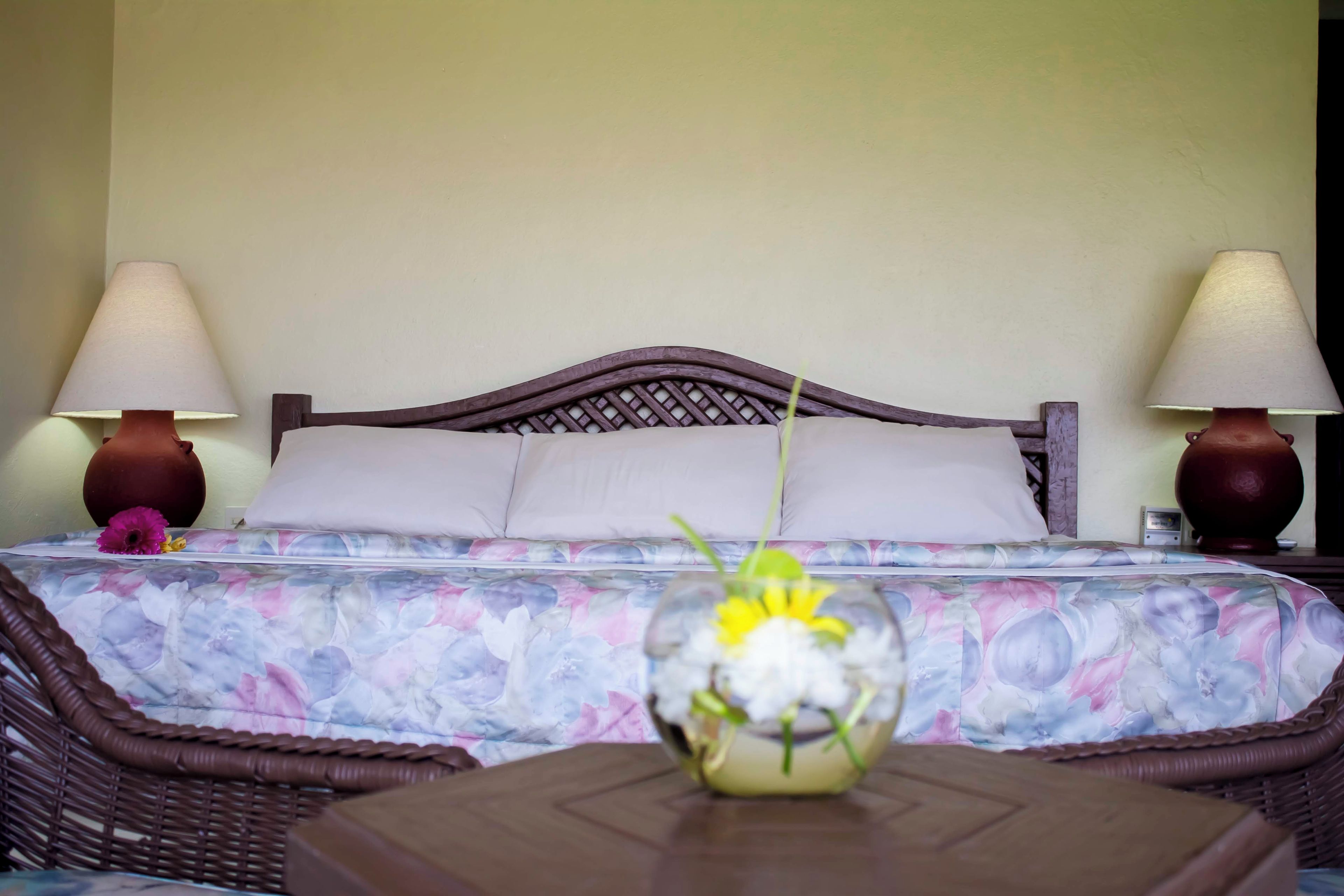 A hotel room with a bed, two bedside lamps, a floral bedspread, and a vase with flowers on a table.