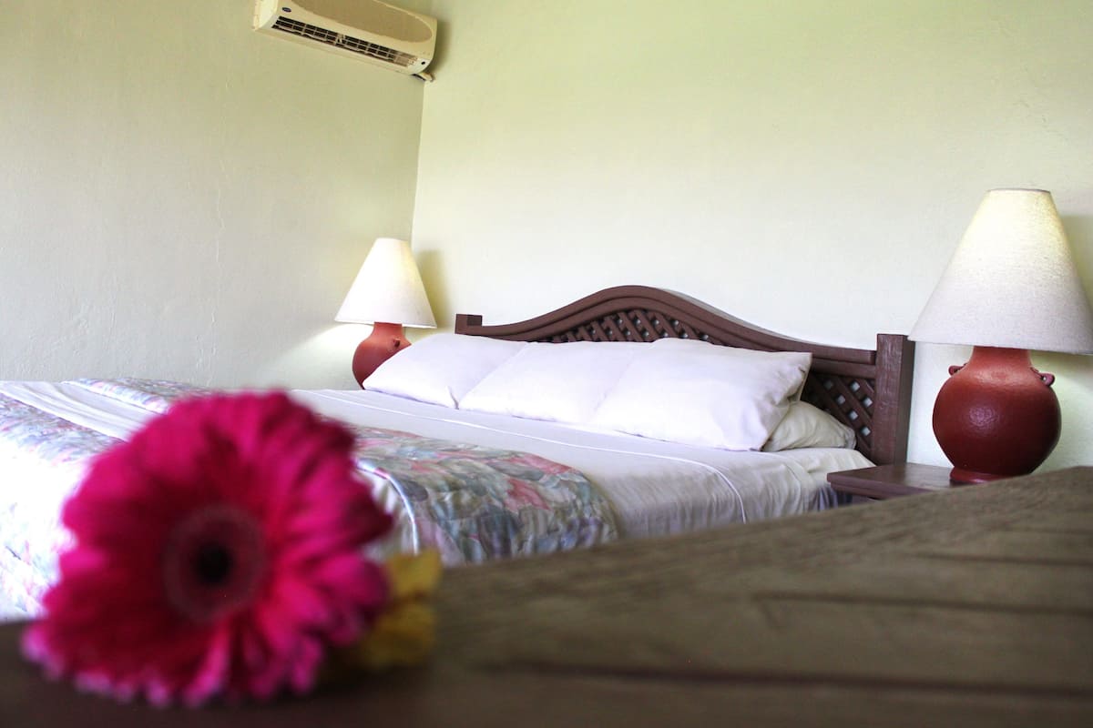 Een hotelkamer met een bed, twee bedlampen, een bloemenbedekking en een rode vaas.