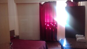 Een hotelkamer met een bed, een bureau, een stoel, een kledingkast en een raam met rode gordijnen.