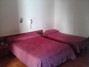 Una habitación con dos camas, cada una con una manta roja, una mesita de noche y un teléfono en la pared.