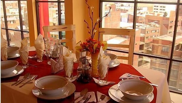 A dining table set for four with white plates, silverware, and a vase with flowers. - Hotel Ensueños (La Paz)