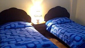 Two twin beds with blue patterned bedding, a bedside table with a lamp, and a wooden floor. - Hotel Ensueños (La Paz)