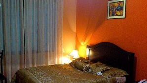 A hotel room with a bed, a nightstand, a lamp, and a painting on the wall. - Hotel Ensueños (La Paz)