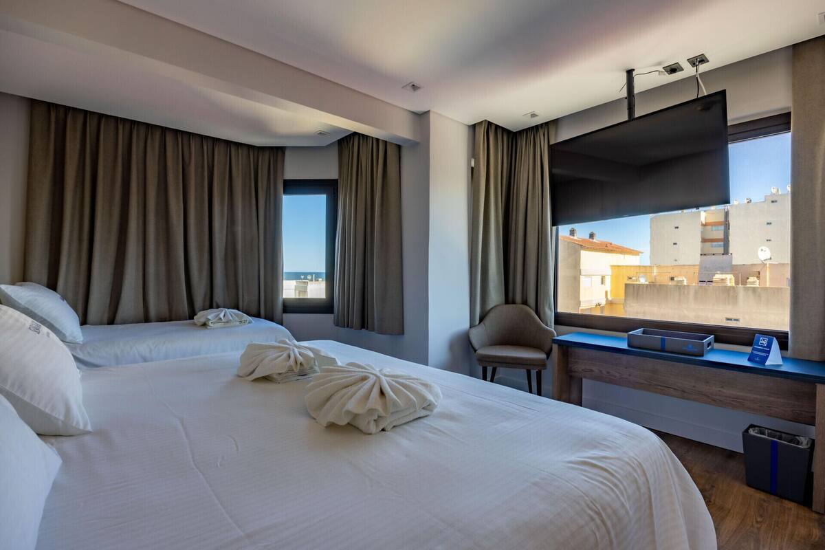 Camera d'albergo con due letti, una sedia, una TV e una finestra vista edifici e mare.