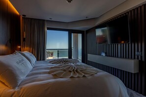 Ett hotellrum med en stor säng, en platt-TV som är monterad på väggen och utsikt över havet genom ett stort fönster.