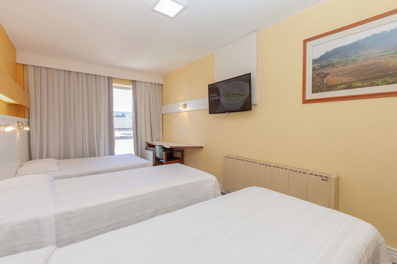 Ein Hotelzimmer mit zwei Betten, einem Schreibtisch, einem Stuhl, einem Fernseher und einem Fenster mit Vorhängen.