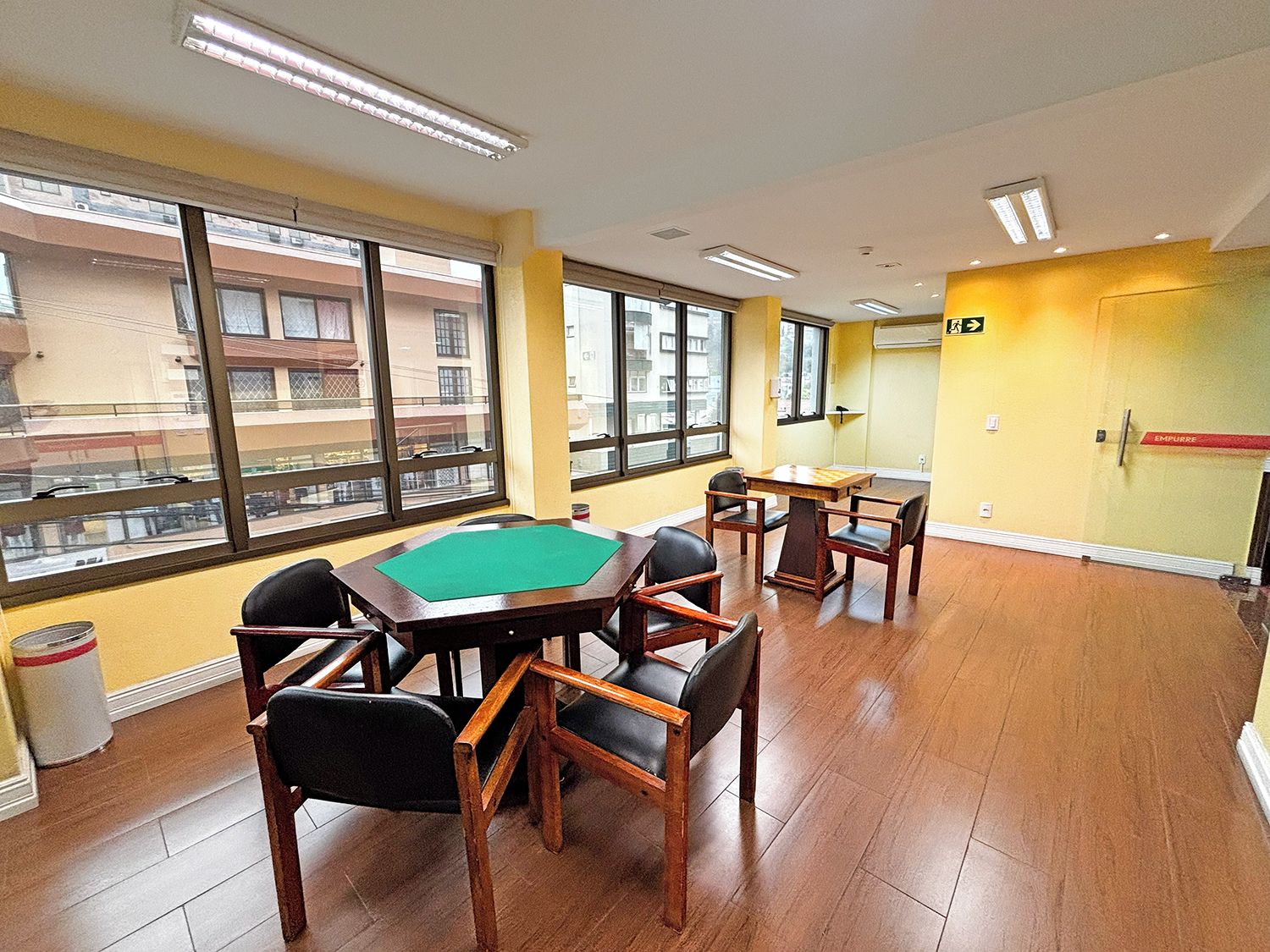 A room with a pool table, chairs, and large windows with a view of buildings.