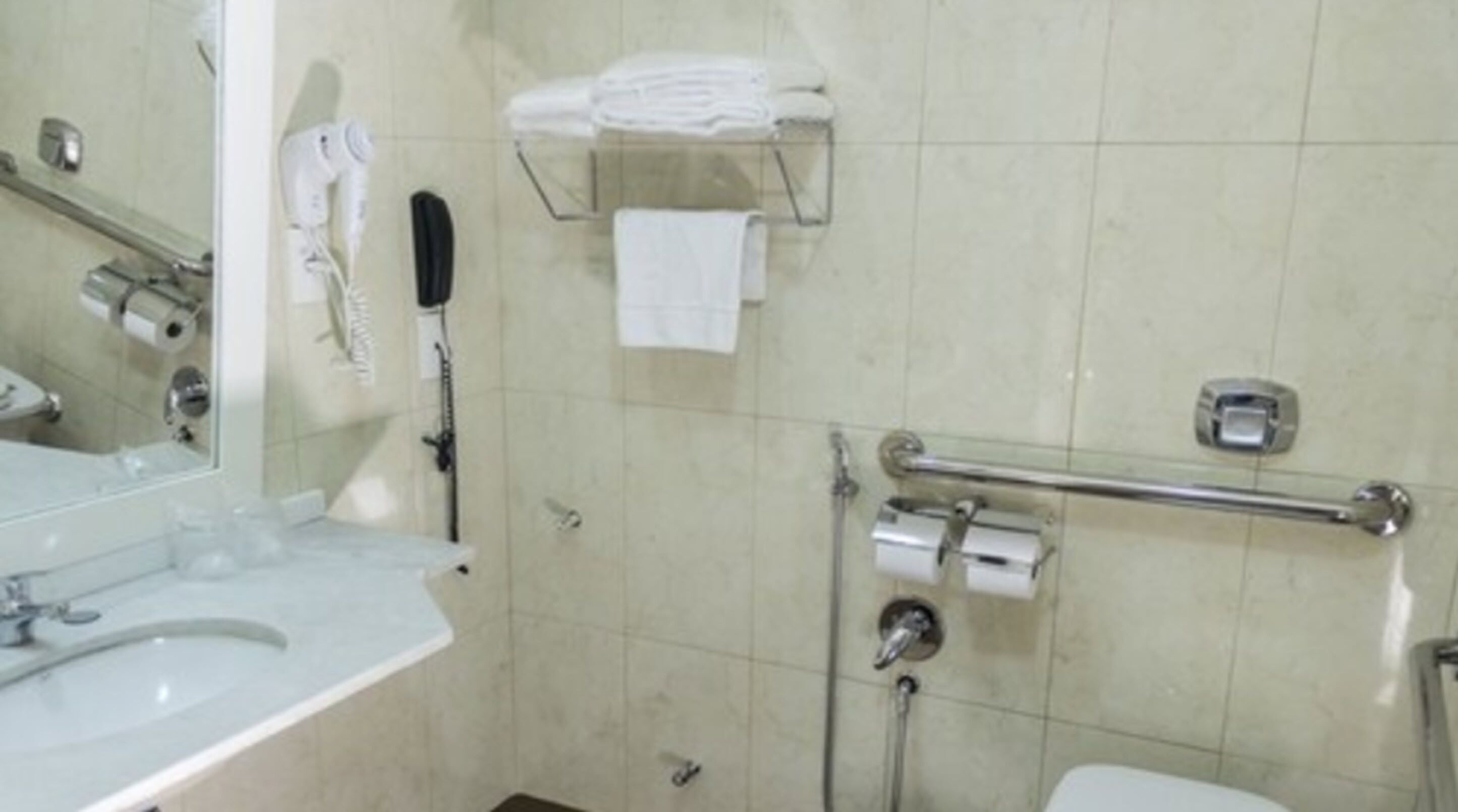 Une salle de bain équipée d’un lavabo, d’un miroir, d’un porte-serviettes, d’un sèche-mains et de toilettes.