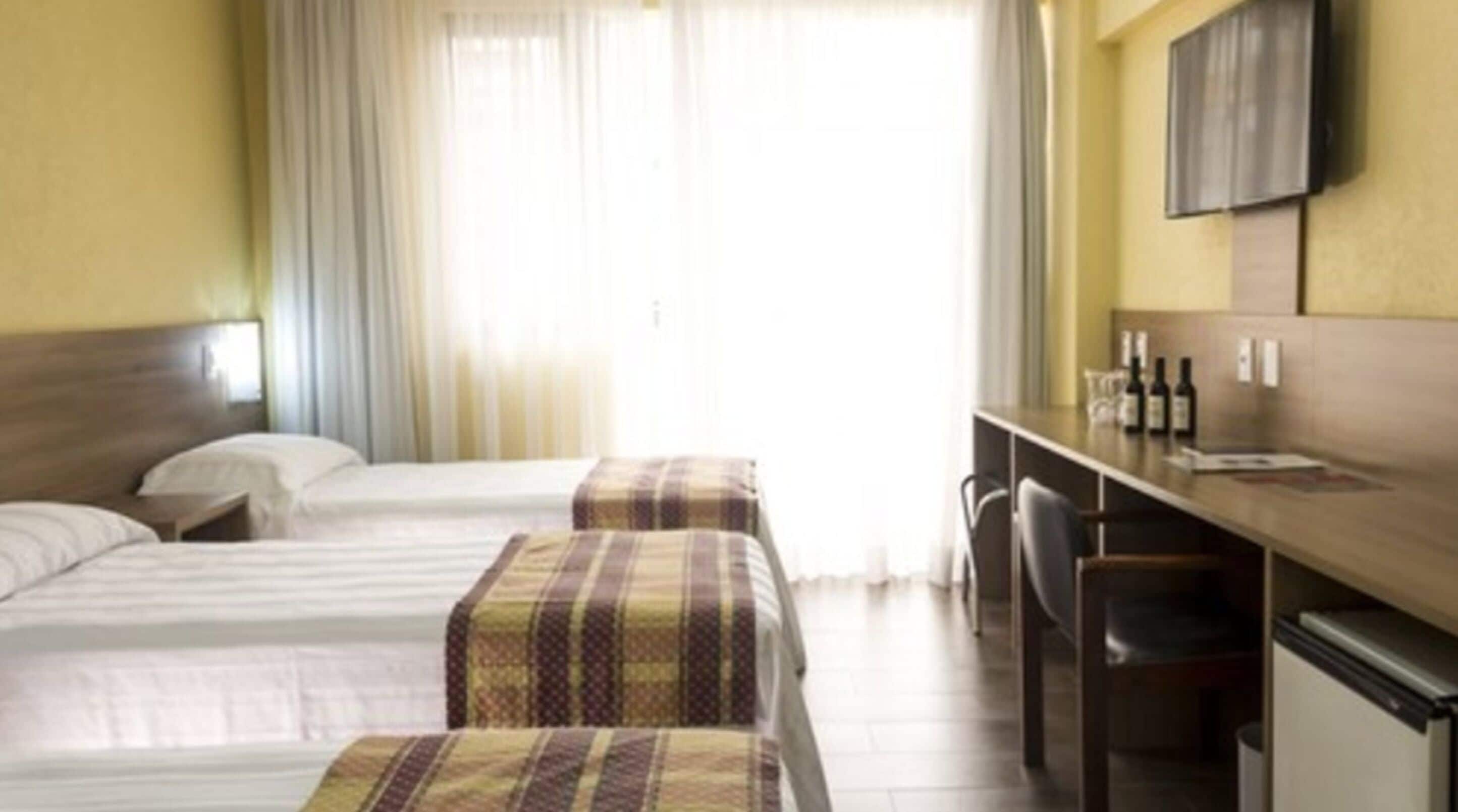 A hotel room with two beds, a desk with chairs, a television, and a minibar.