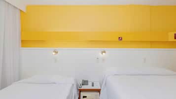Habitación de hotel con dos camas individuales, una mesita de noche con teléfono y radio, y una pared de acento en color amarillo.
