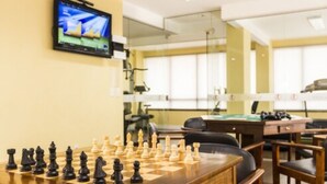 Un tablero de ajedrez dispuesto sobre una mesa de madera en una habitación con un televisor montado en la pared.