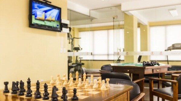 Un tablero de ajedrez dispuesto sobre una mesa de madera en una habitación con un televisor montado en la pared.