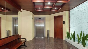 Un pasillo con un banco, un ascensor y un panel de vidrio decorativo en la pared.