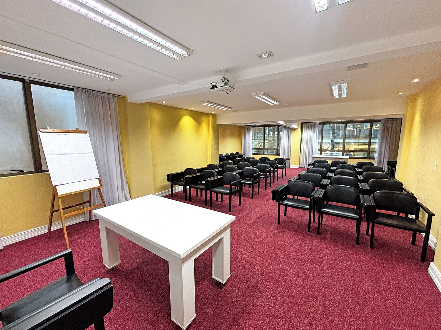 Ein Konferenzraum mit einer Tafel, einem Projektor und Reihen schwarzer Stühle.