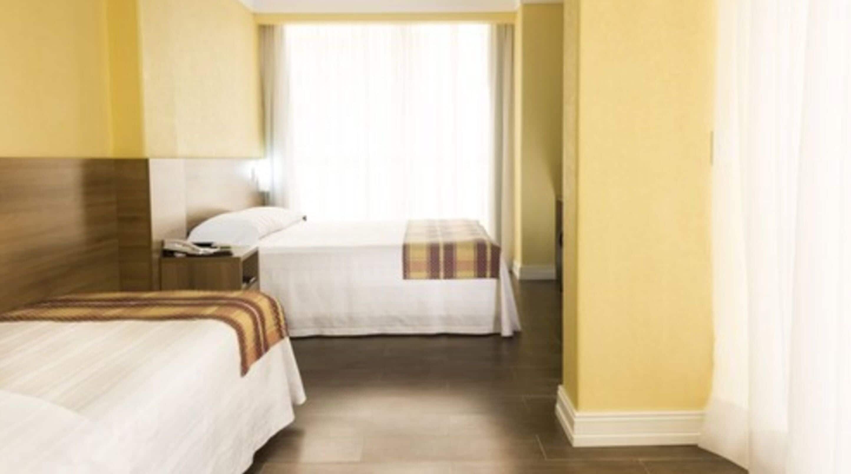 Een hotelkamer met twee bedden, een houten hoofdbord, een nachtkastje en een raam met gordijnen.