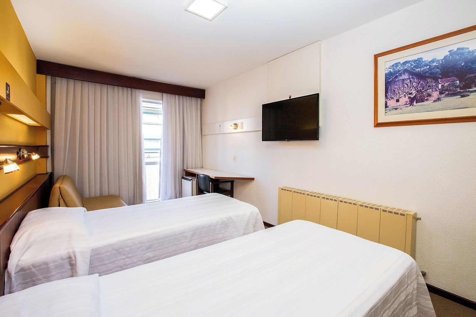 Une chambre d’hôtel avec deux lits, un bureau, une chaise, une télévision et un tableau au mur.