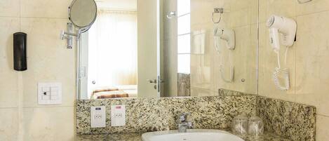 A bathroom with a granite countertop, a white sink, a mirror, a hairdryer, and a telephone.