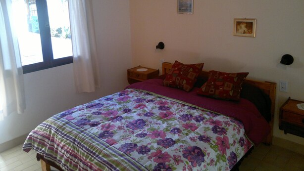 A bedroom with a bed, two nightstands, a window with curtains, and two wall-mounted lamps.
