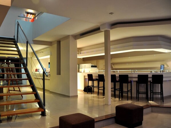 A modern interior with a staircase, a bar area with stools, and a high ceiling. - Piazza Hotel (Villa Carlos Paz)