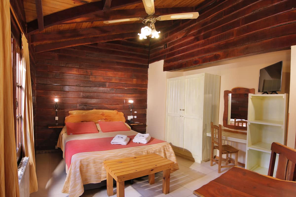Una habitación tipo cabaña de madera con una cama, un banco de madera, una mesa y una silla.