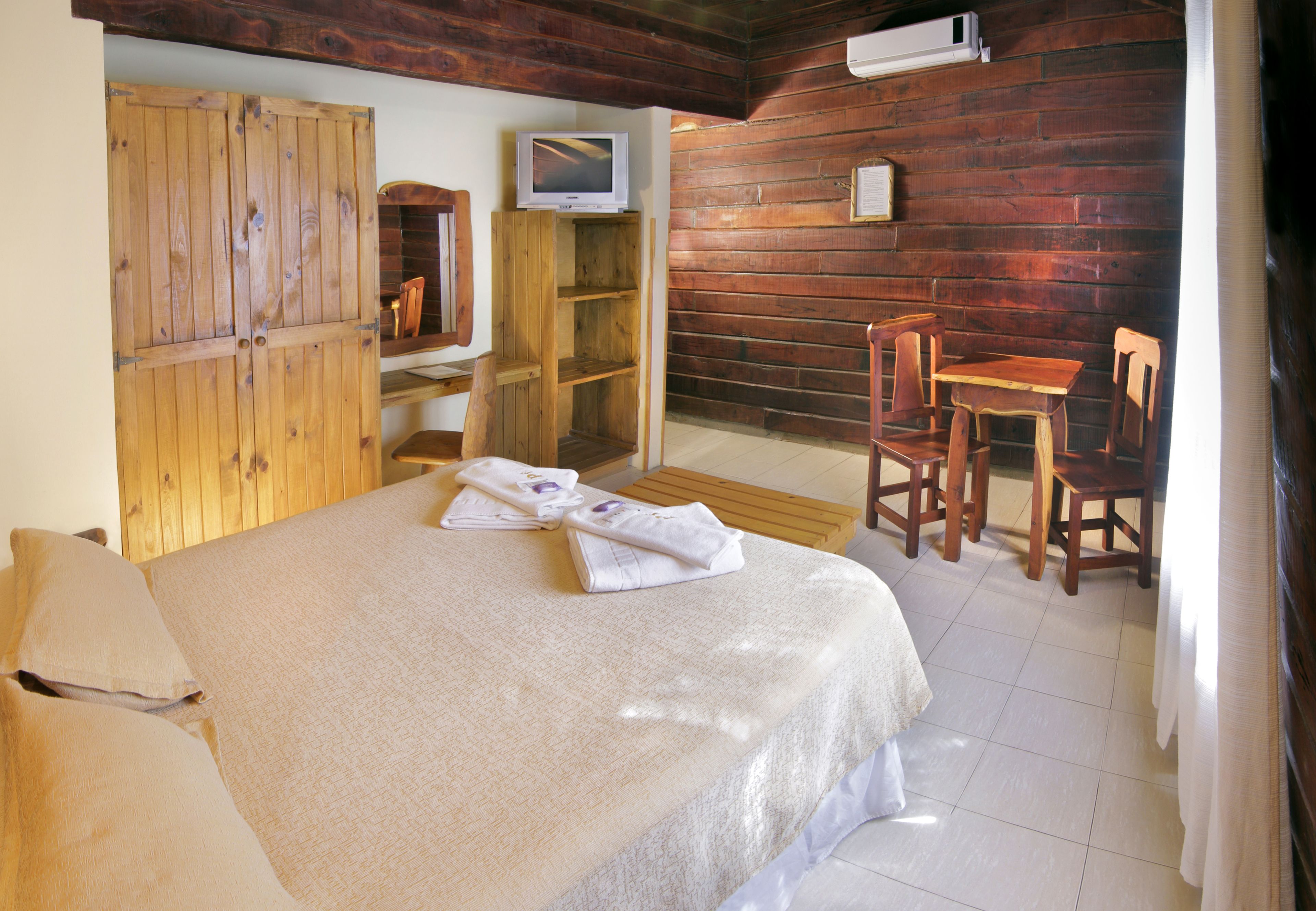 A bedroom with a bed, wooden wardrobe, television, and a small table with chairs.