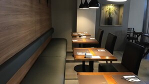 Un interior de restaurante moderno con paredes de madera, sillas negras y mesas dispuestas con servilletas y cubiertos blancos.