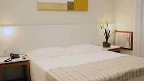 Habitación de hotel con cama, mesita de noche, lámpara y una obra de arte colgada en la pared.