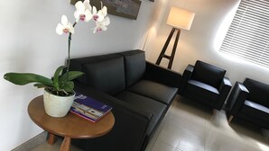 Una sala de estar moderna con un sofá negro, una pequeña mesa redonda de madera con una planta en maceta y un libro, una lámpara de pie y dos sillones negros.