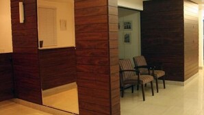 Una zona de recepción con mostrador de madera, un espacio de espera con sillas y un panel de vidrio.